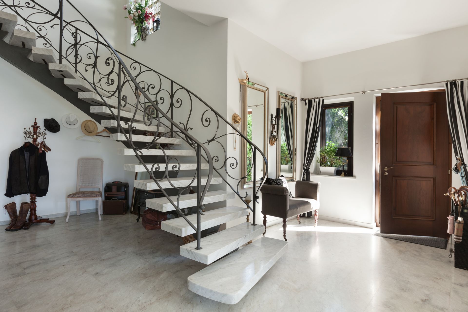 Un escalier en marbre avec une rampe en fer forgé ouvragée dans une entrée lumineuse.