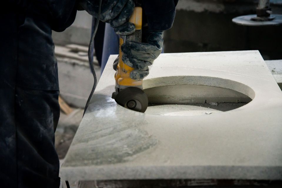 Une personne utilise un outil électrique pour découper une forme circulaire dans une surface en pierre blanche.