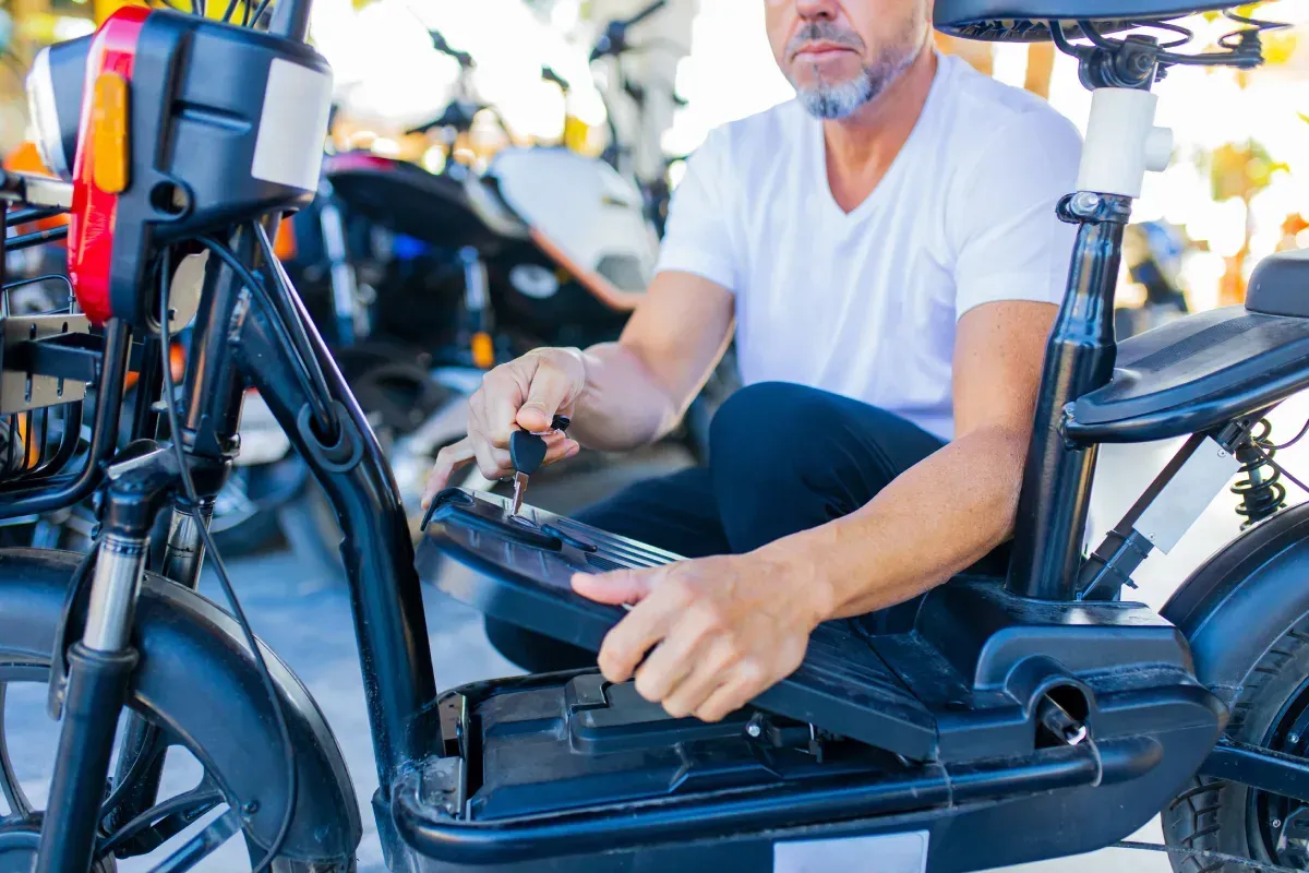 Hombre con camisa blanca trabajando en una bicicleta eléctrica, posiblemente reemplazando la batería, al aire libre.