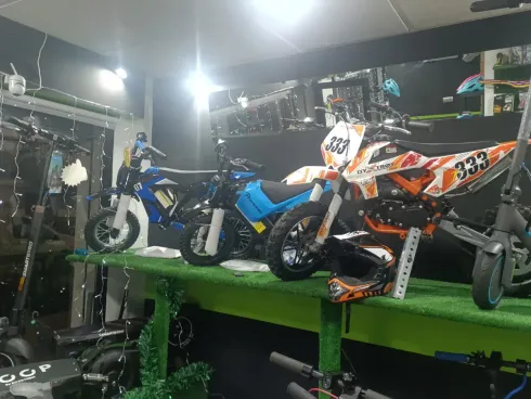 Motocicletas en exhibición dentro de una tienda, con mesa verde y mercancía variada.