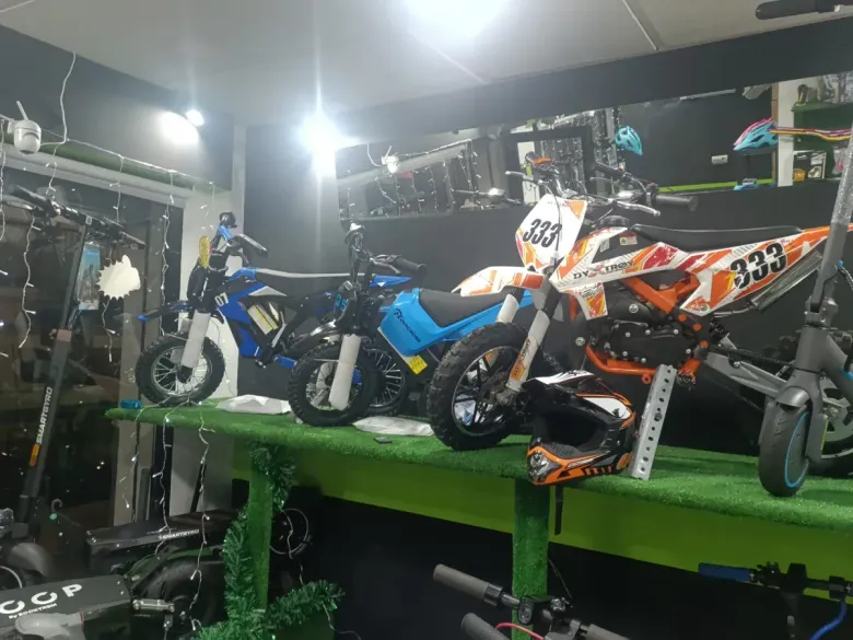 Motocicletas en exhibición dentro de una tienda, con mesa verde y mercancía variada.