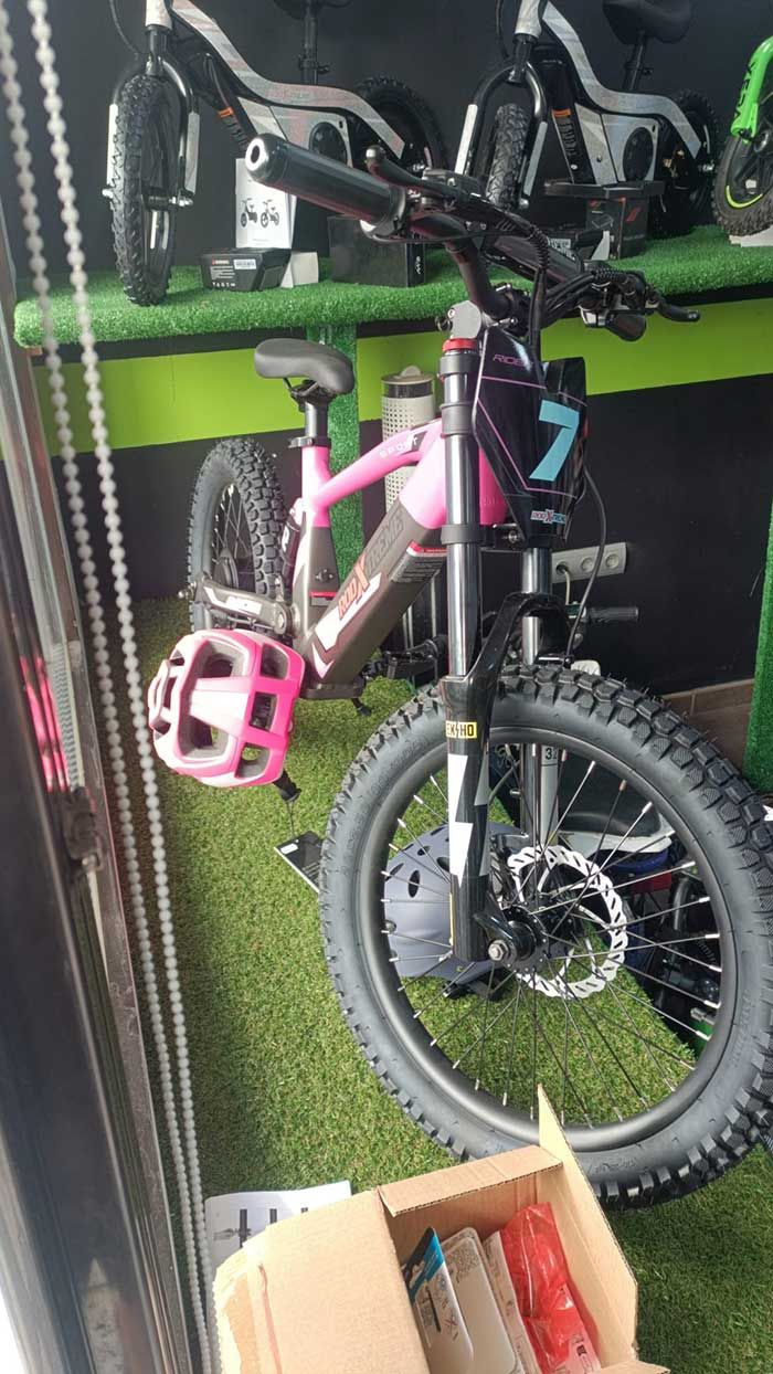 Bicicleta infantil rosa con ruedines y casco rosa en el escaparate de una tienda de bicicletas.