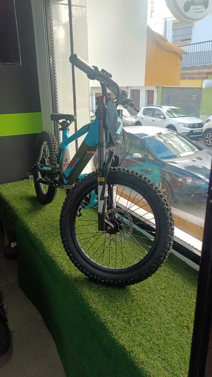 Bicicleta de montaña negra con detalles en color turquesa expuesta en el interior, junto a una ventana.