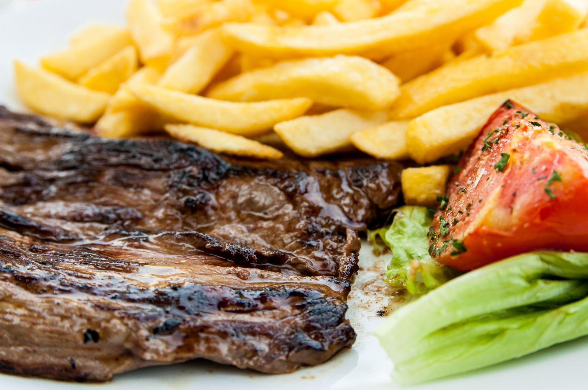 Bistec a la parrilla con patatas fritas, tomate y lechuga en un plato blanco.