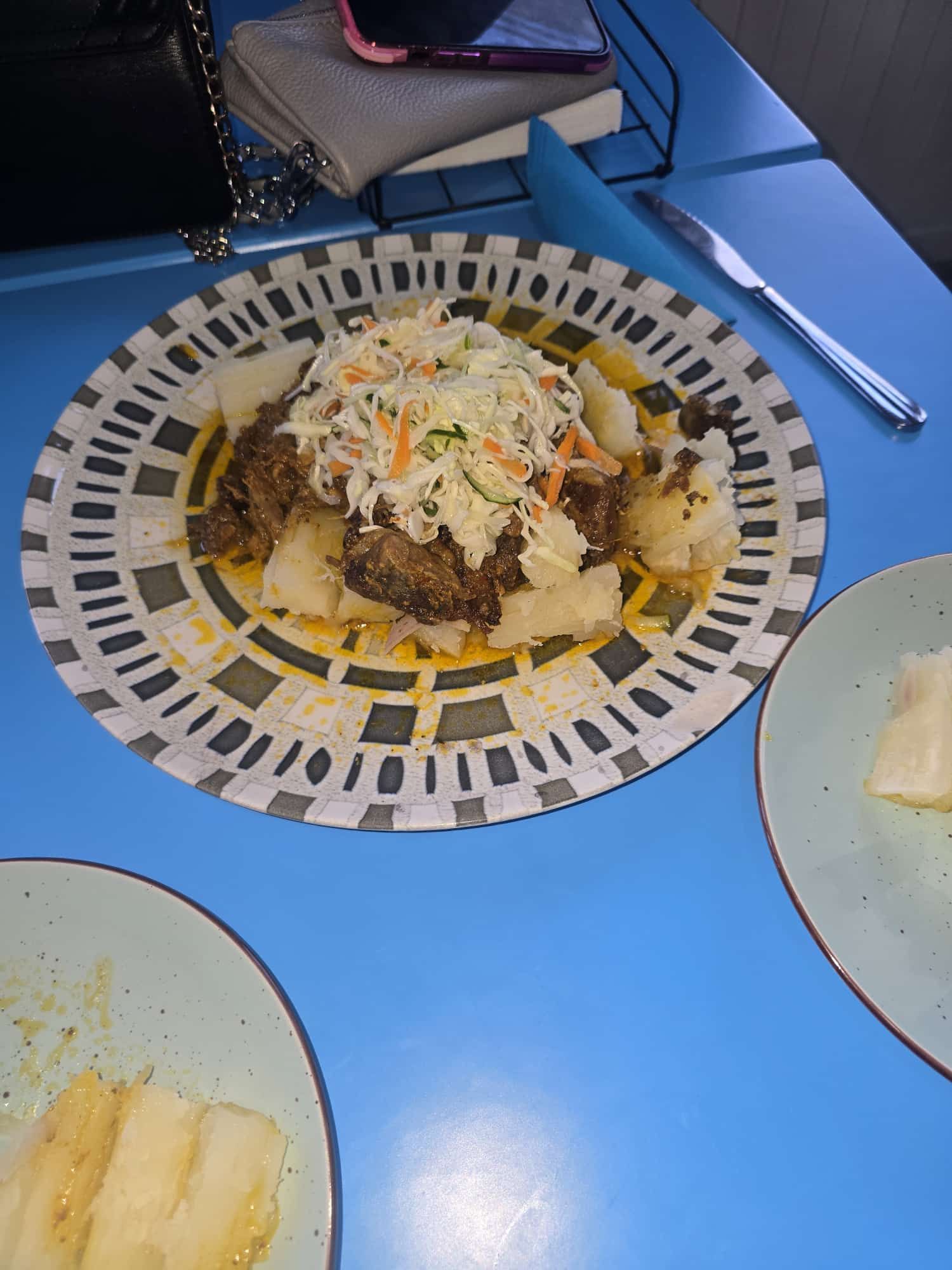 Un plato con carne, patatas y ensalada de col, sobre una mesa azul. Otro plato con patatas.