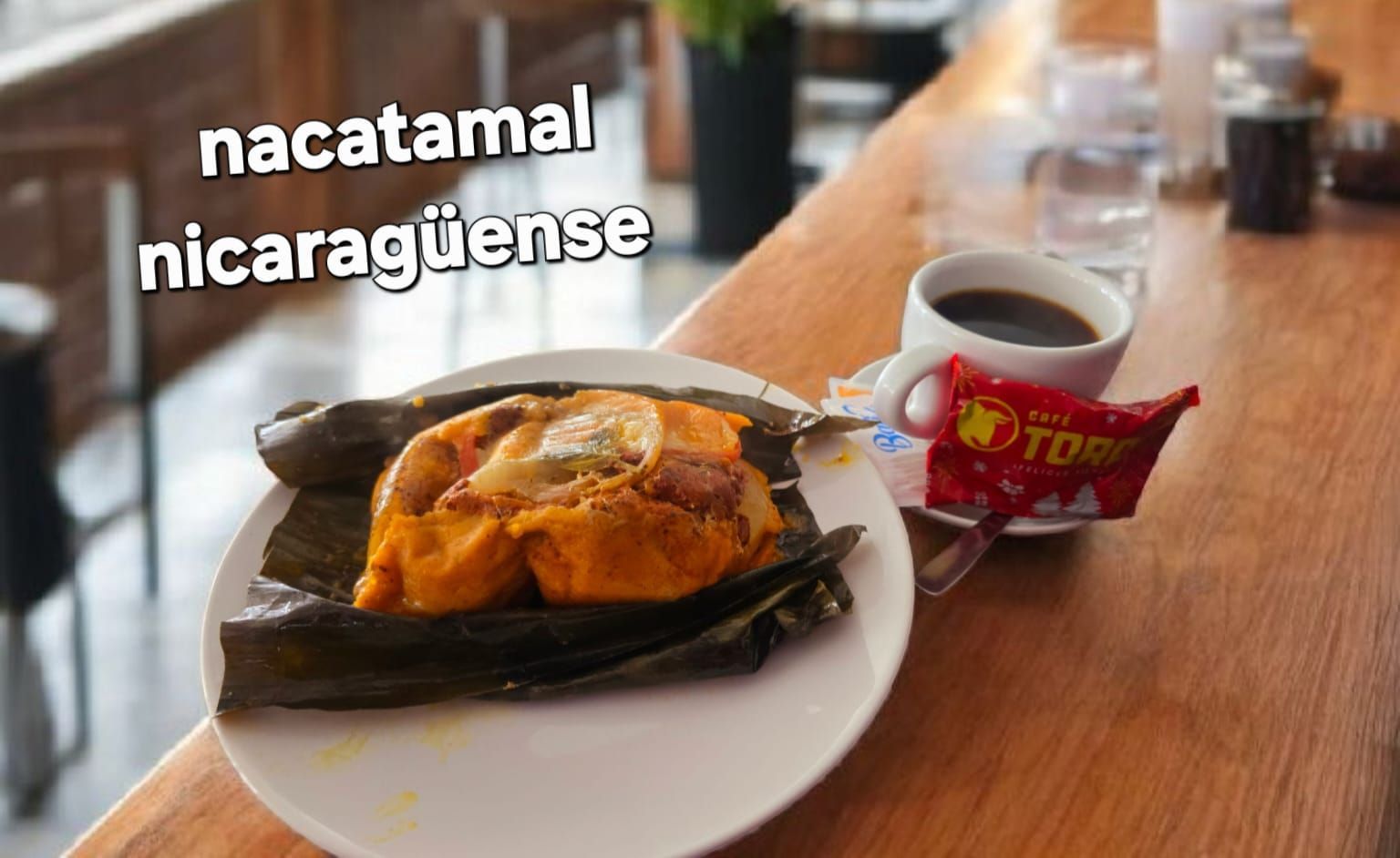 Nacatamal en un plato con café, un pequeño paquete de salsa roja y una mesa de madera.
