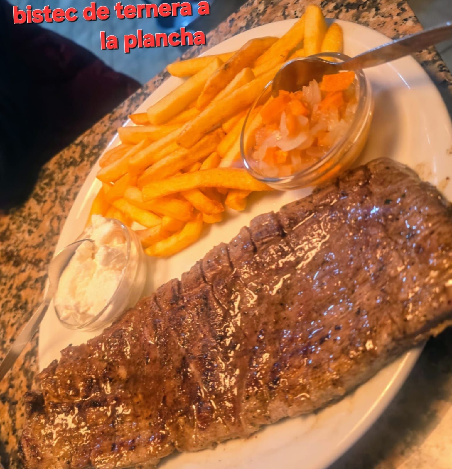 Bistec a la parrilla con patatas fritas y verduras en un plato blanco.