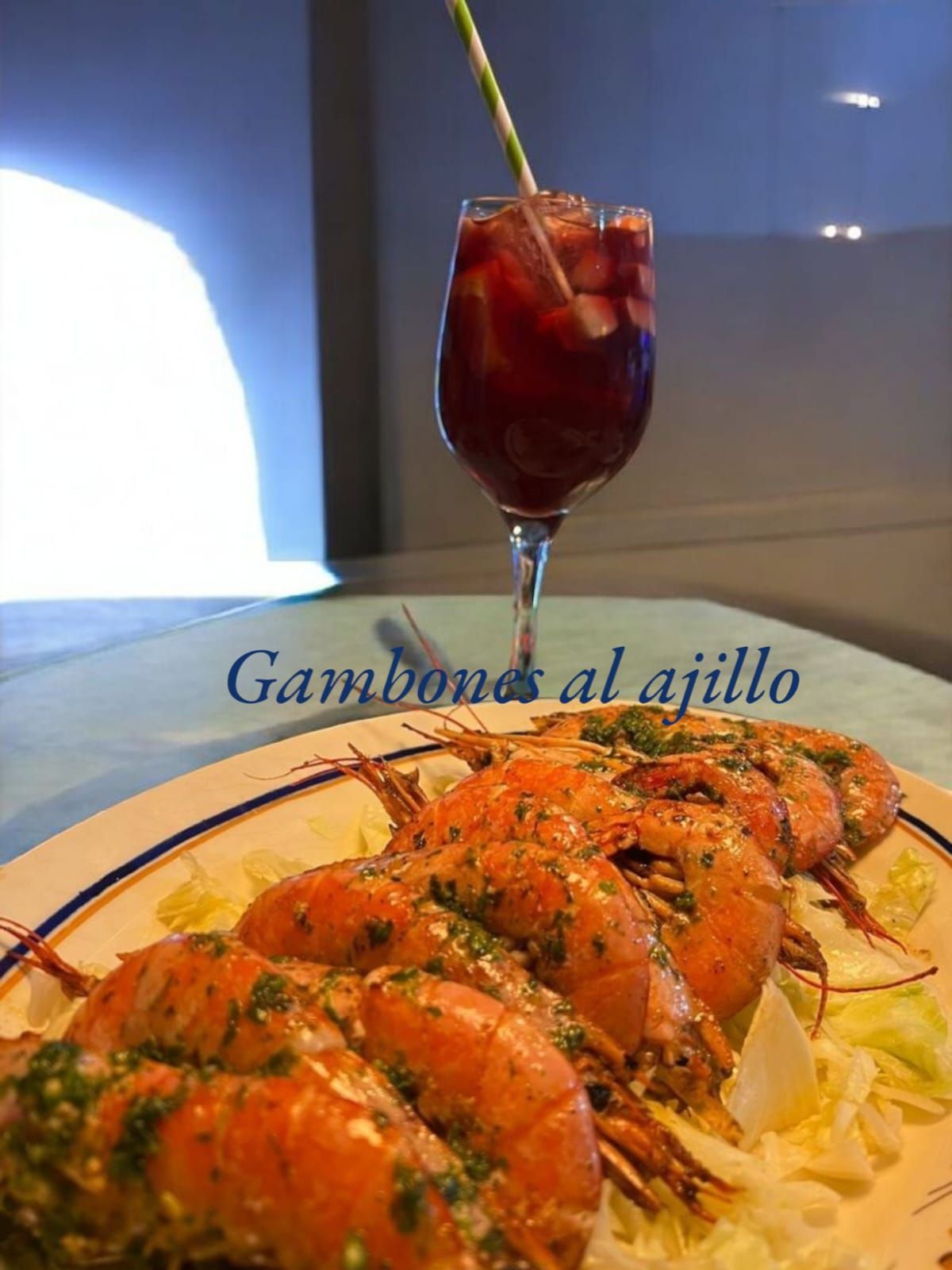 Gambones al ajillo, camarones al ajillo españoles, en un plato con un vaso de sangría.