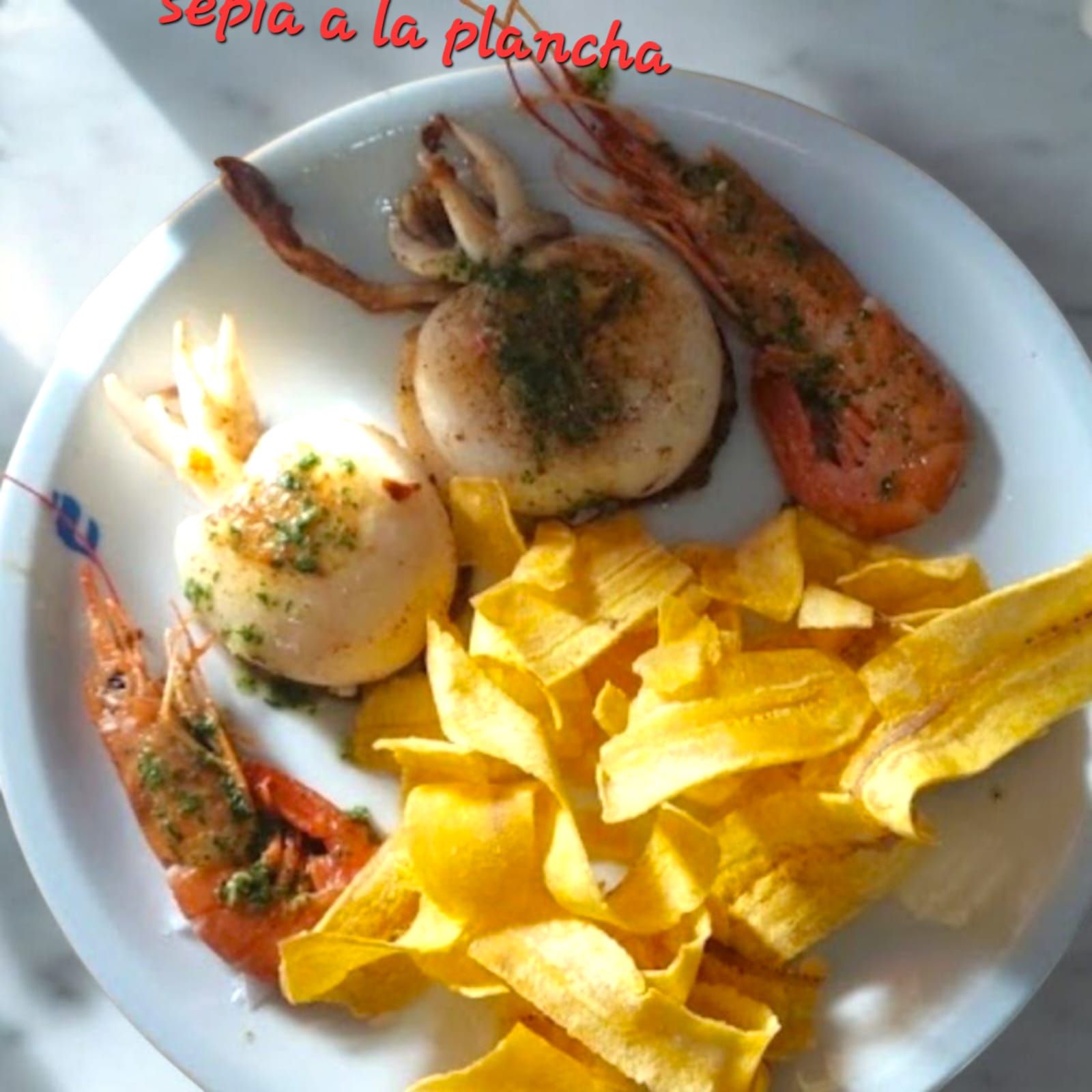 Sepia y camarones a la plancha con chips de plátano en un plato blanco.