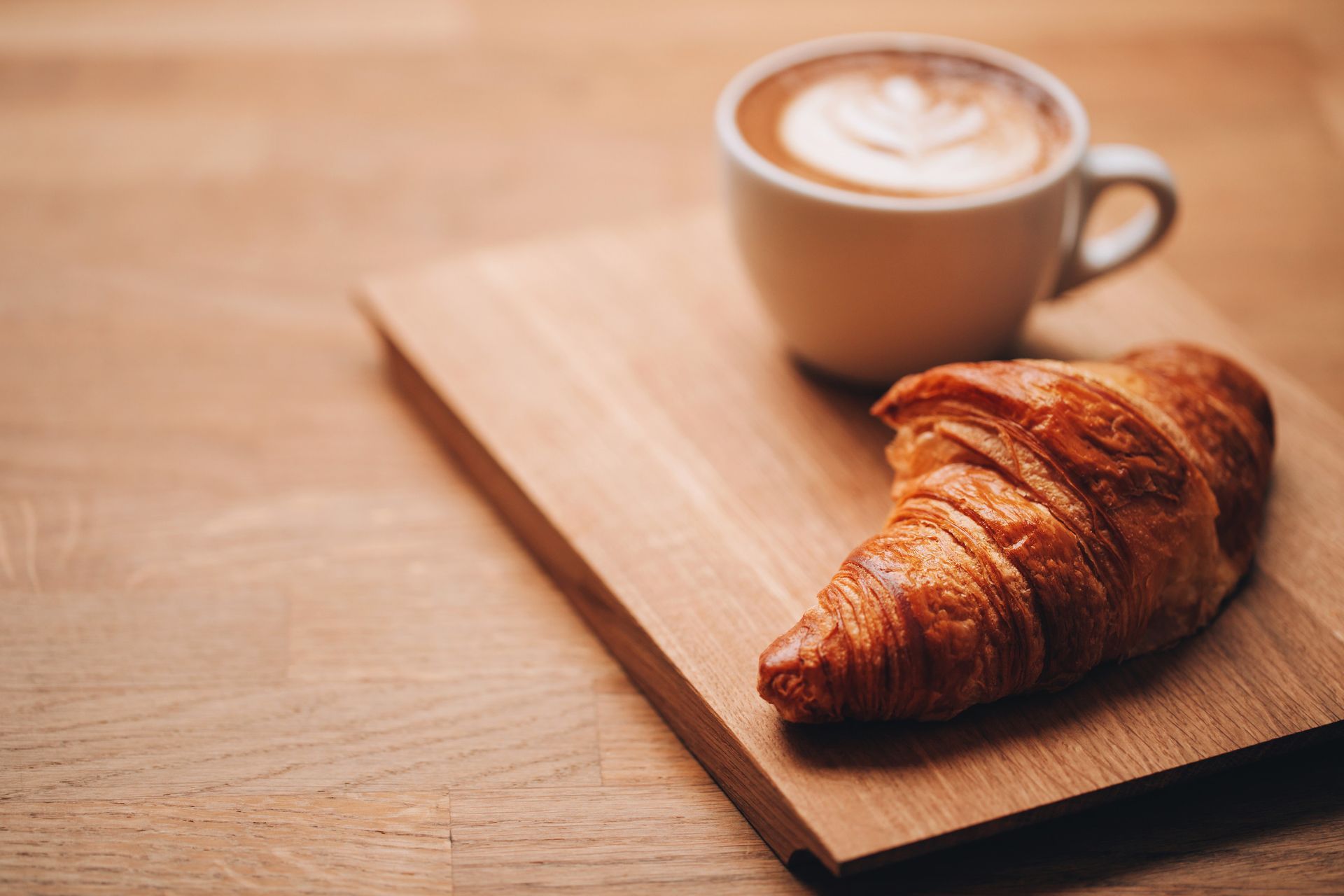 Croissant y café con leche sobre una tabla de madera.