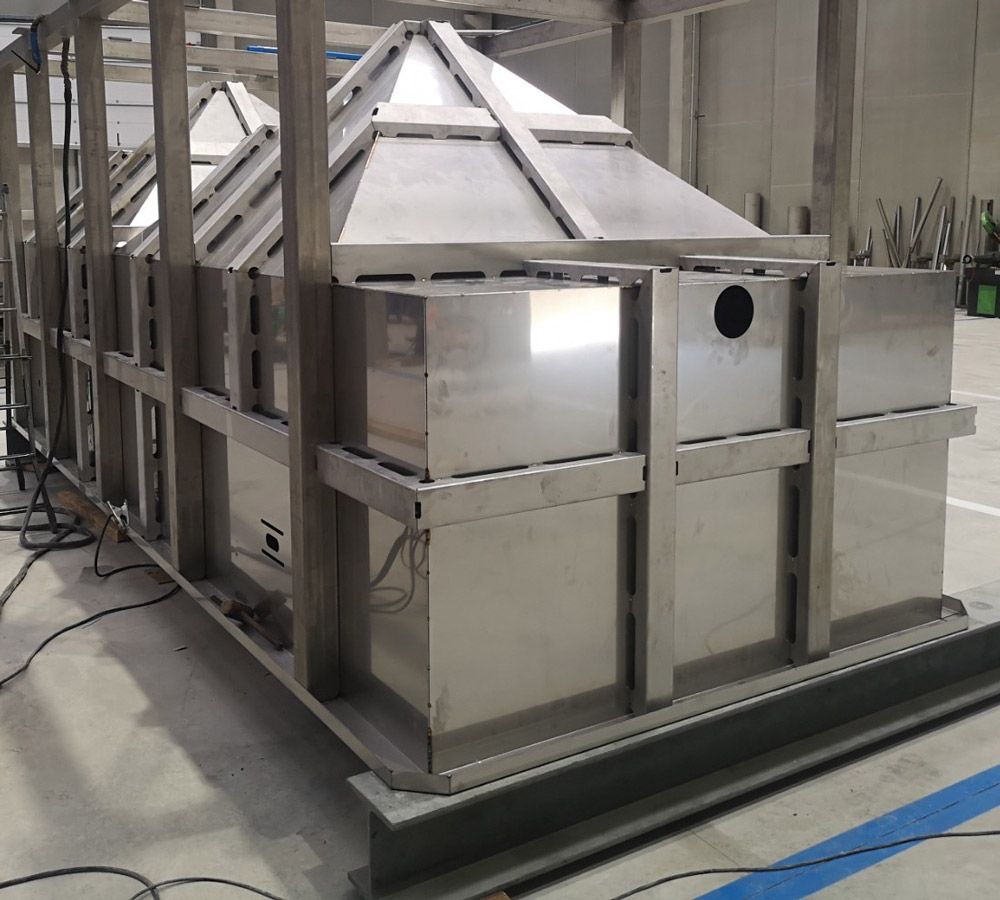 Gran estructura rectangular de acero inoxidable con techos en forma de pirámide en el interior de una fábrica.