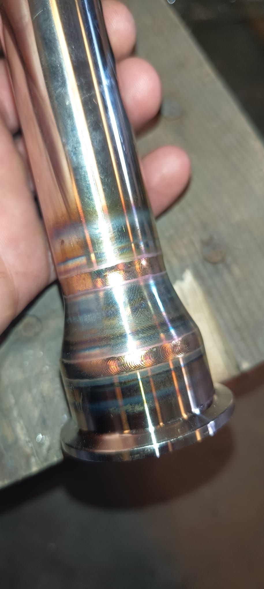 Se sostiene un objeto metálico brillante en una mano. Presenta marcas de calor de colores.