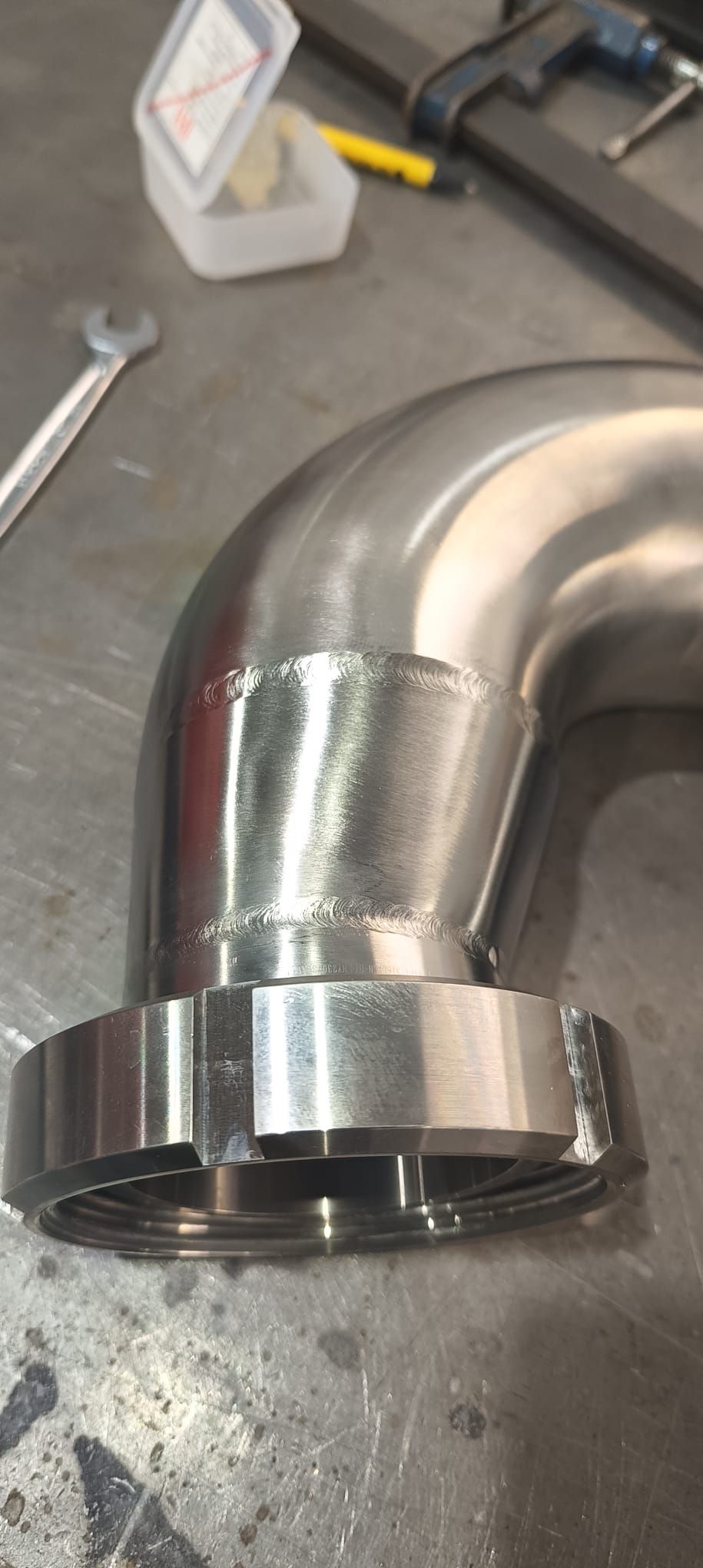 Un codo de tubería de metal con una base de brida sobre una superficie metálica.