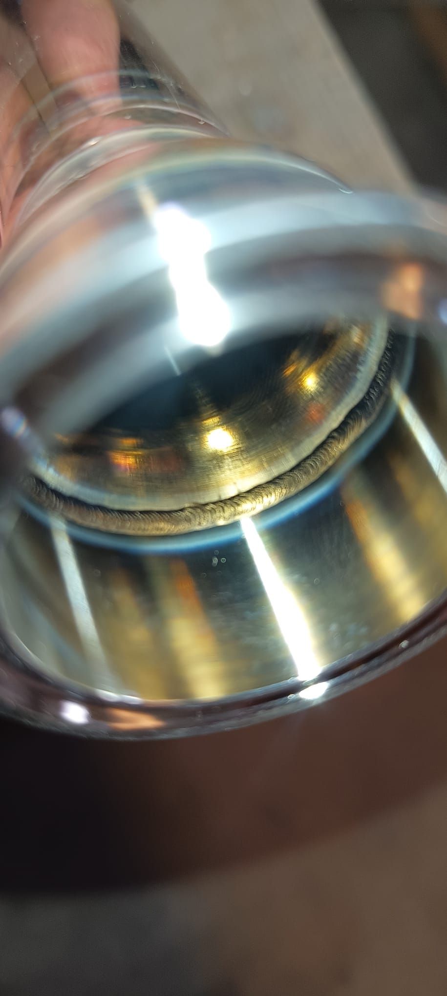 Mirando dentro de una tubería de metal brillante, mostrando una soldadura y una superficie interior.