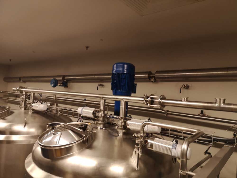 Tanques de acero inoxidable con tuberías y motor azul en entorno de fábrica.