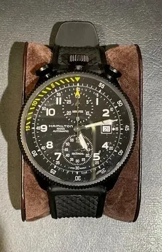 Un reloj negro con una correa marrón está sobre una mesa.