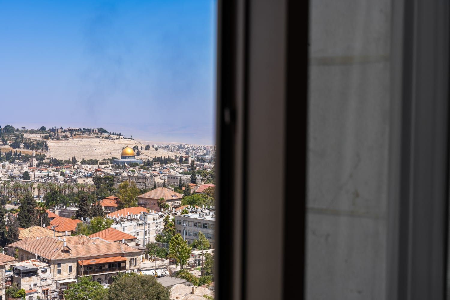 A view of a city from a window with a view of the dome of the rock.