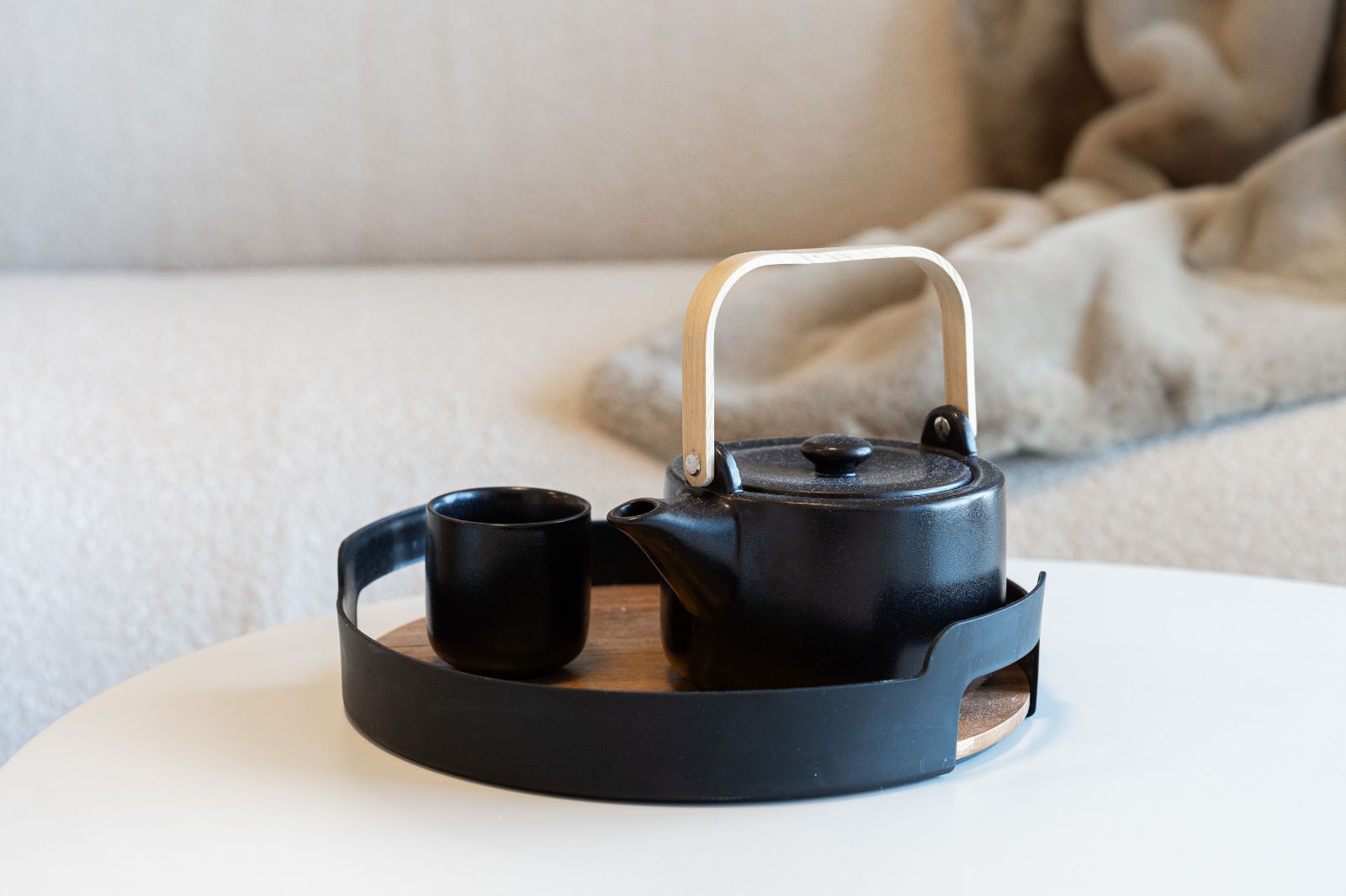 A black teapot and two cups are on a tray on a table.