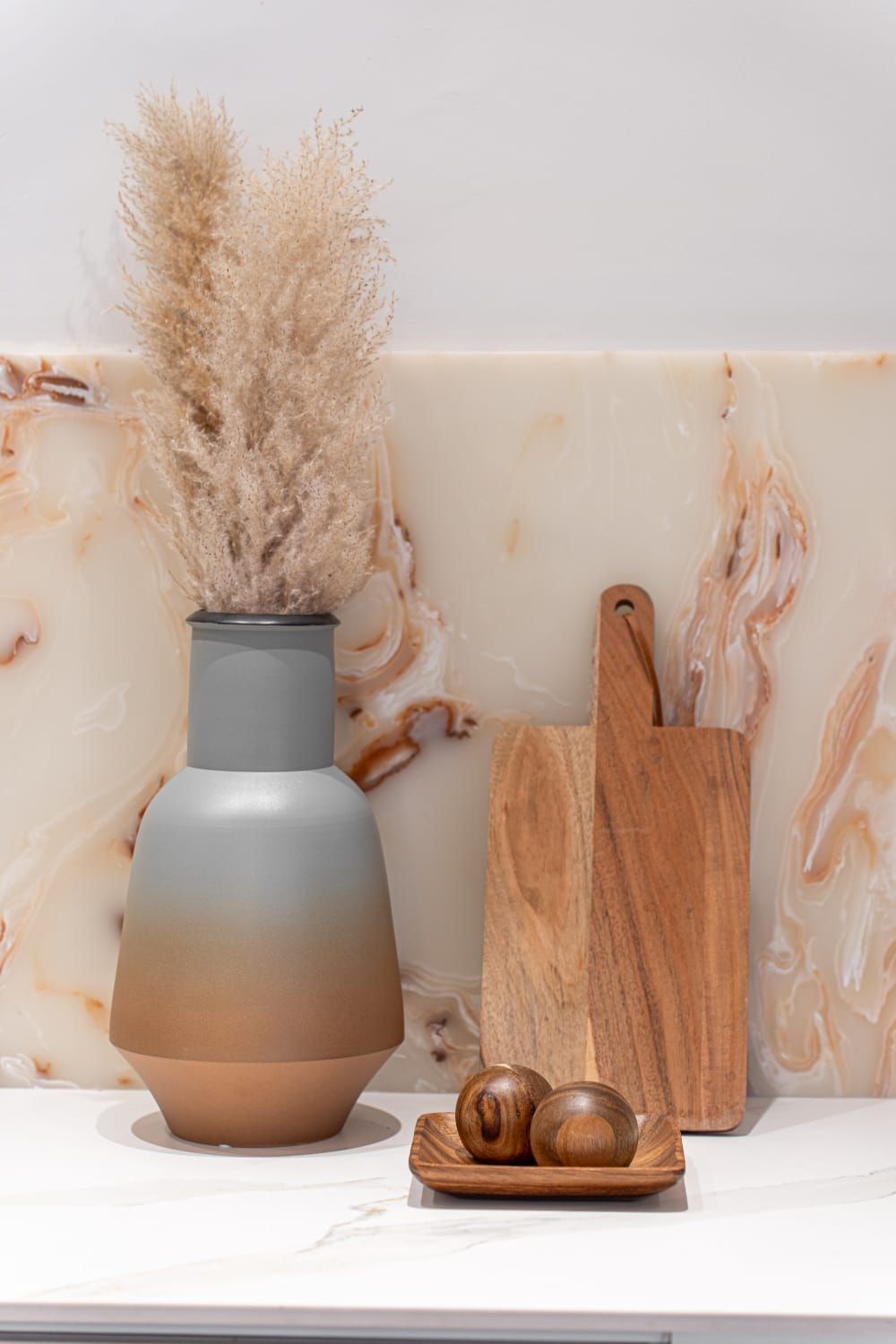 A vase with dried flowers in it is sitting on a counter next to a wooden cutting board.