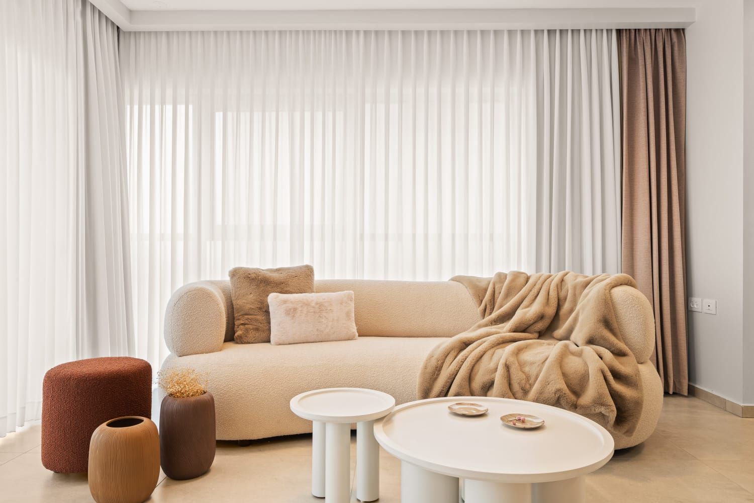 A living room with a couch , tables , ottomans and a large window.