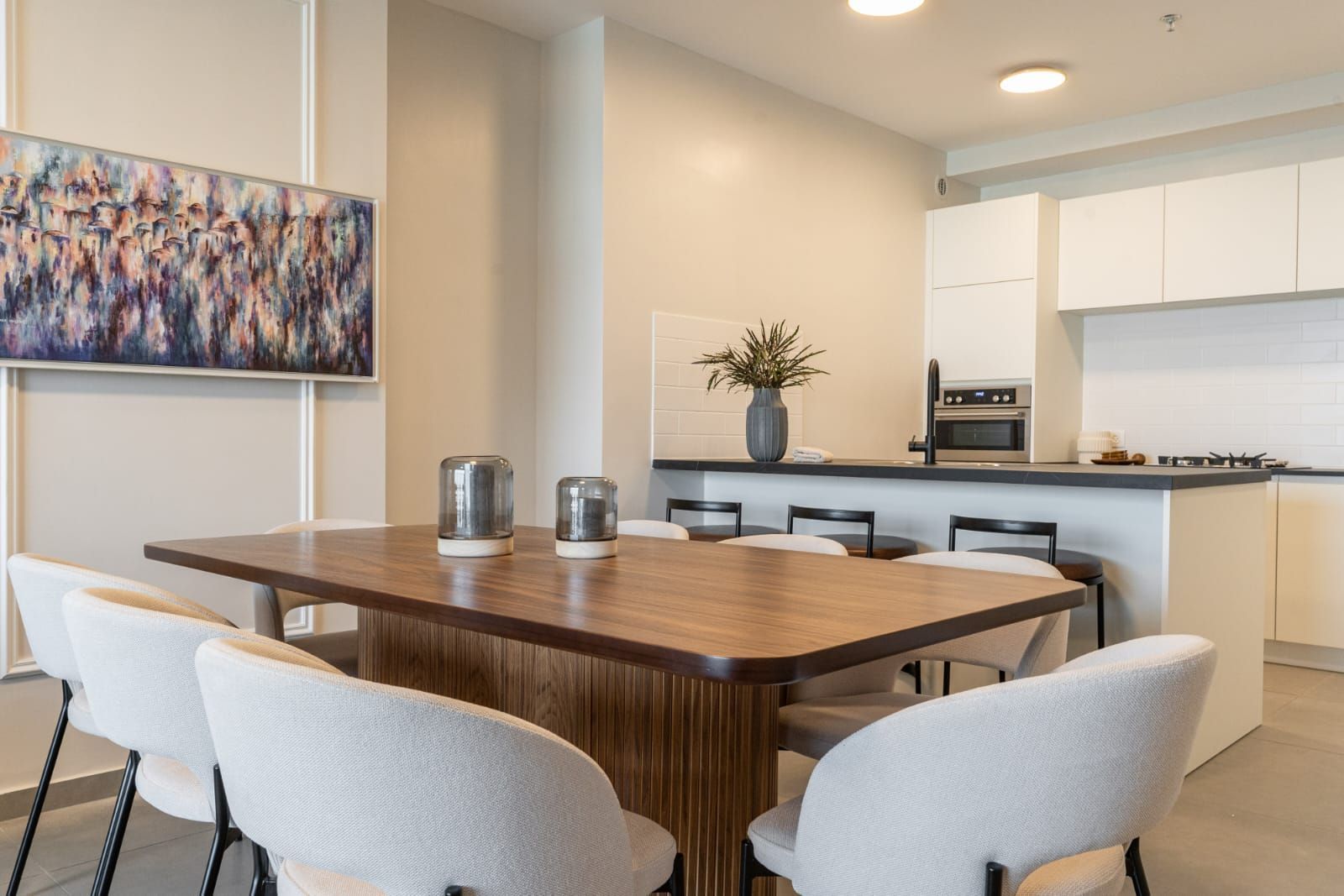 A dining room with a table and chairs and a painting on the wall.