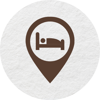 An icon of a bed in a pin on a white background.