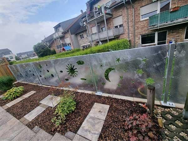 Ein Garten mit einem Zaun und einem Backsteingebäude im Hintergrund.