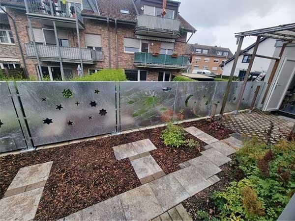 Ein Metallzaun umgibt einen Garten vor einem Gebäude.