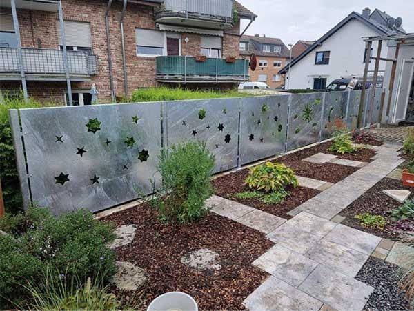 Ein Metallzaun in einem Garten mit einem Haus im Hintergrund.