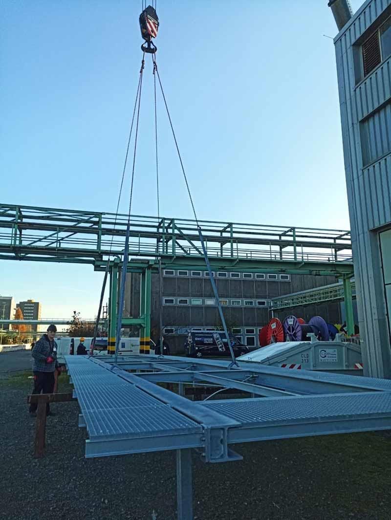 Ein Kran hebt eine Metallkonstruktion vor einem Gebäude an.