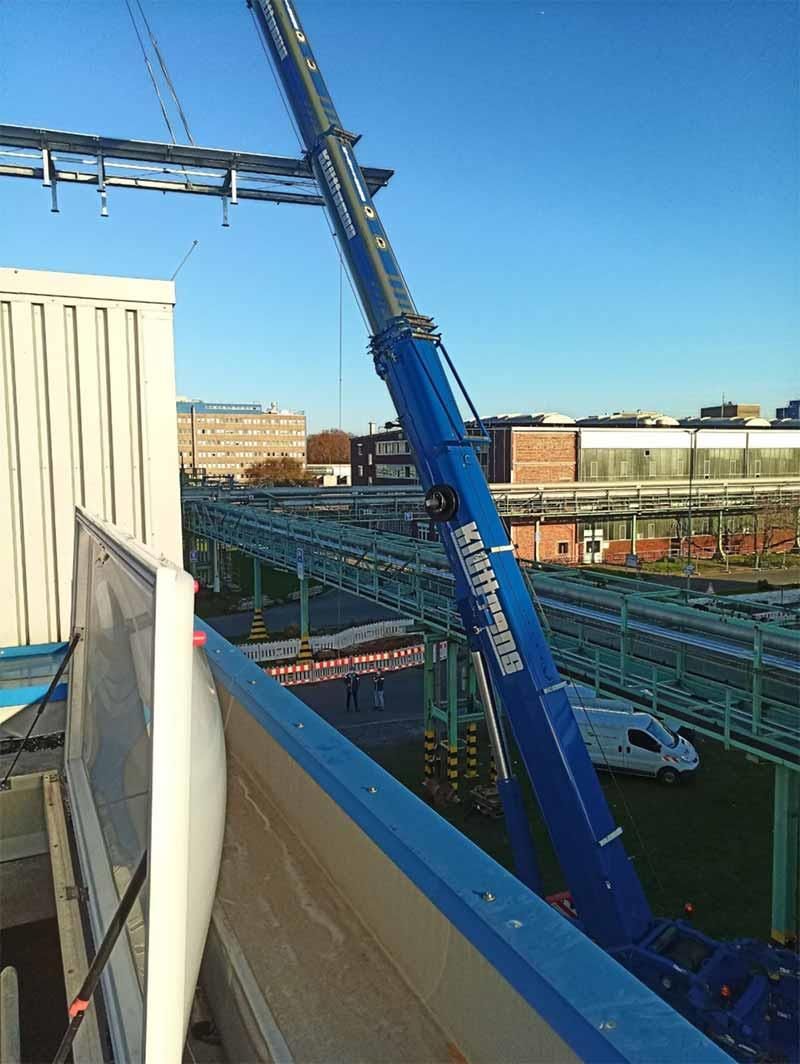 Mit einem großen blauen Kran wird ein Gebäude angehoben.