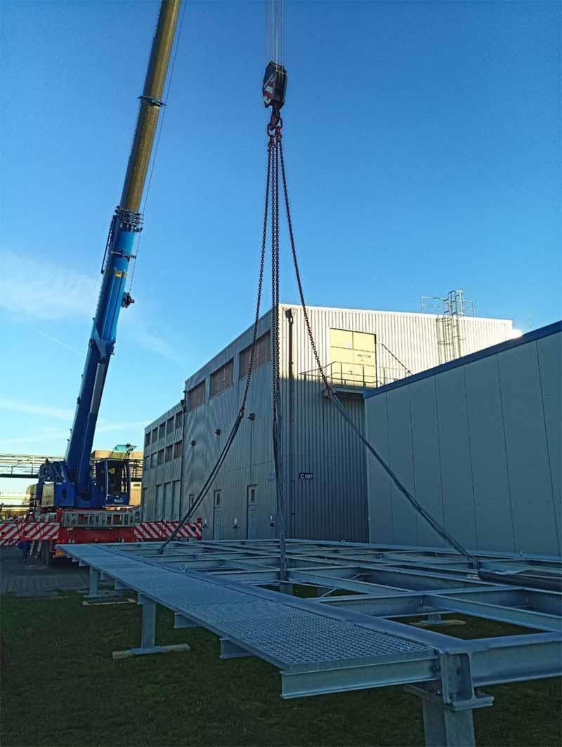 Ein Kran hebt eine Metallkonstruktion vor einem Gebäude an.