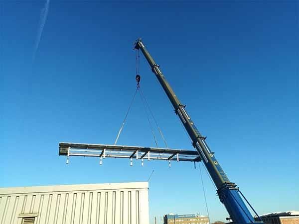 Ein Kran hebt ein großes Stück Metall über ein Gebäude