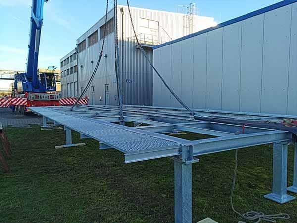 Ein Kran hebt eine Metallkonstruktion vor einem Gebäude an.
