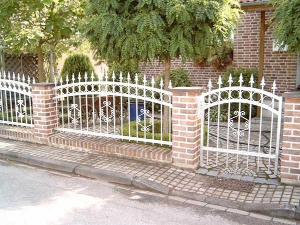 Ein weißer schmiedeeiserner Zaun ist von Ziegelpfeilern umgeben