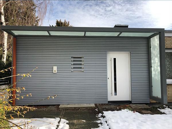 Ein graues Haus mit einer weißen Tür und einem Vordach