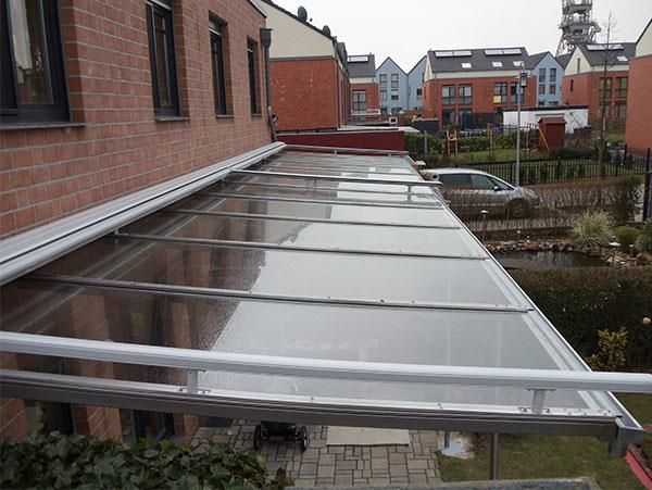 An der Seite eines Backsteingebäudes ist ein durchsichtiges Vordach angebracht.