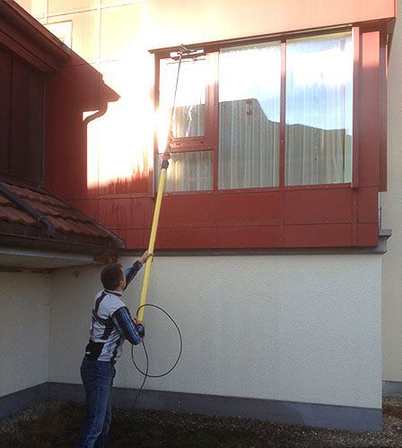 Ein Mann reinigt die Fenster eines Gebäudes mit einem Hochdruckreiniger .