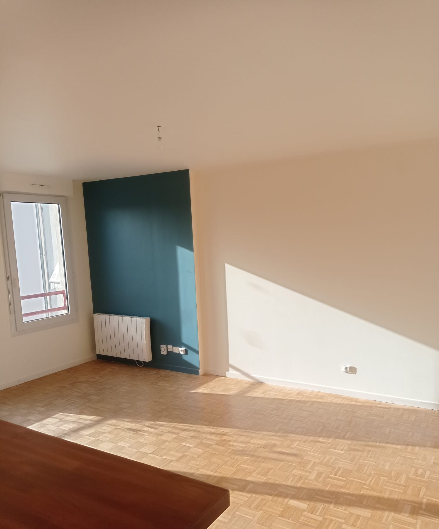 Pièce vide avec un mur d'accent turquoise, des murs beiges et un parquet. La lumière du soleil y pénètre abondamment.
