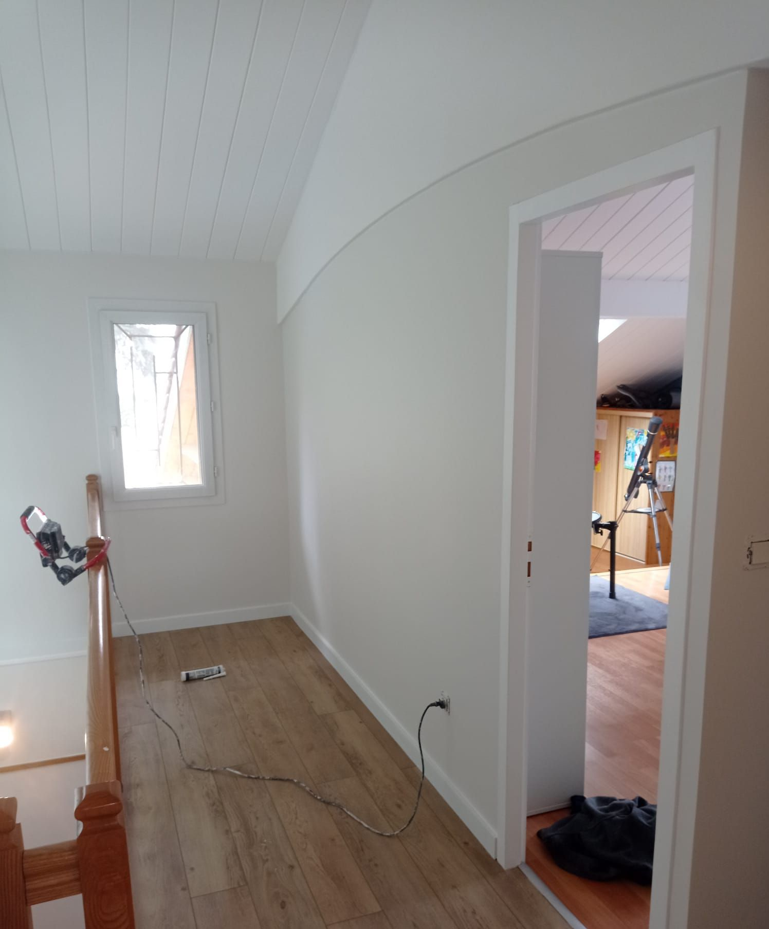 Couloir aux murs blancs, au sol en bois et donnant sur une porte menant à une autre pièce.