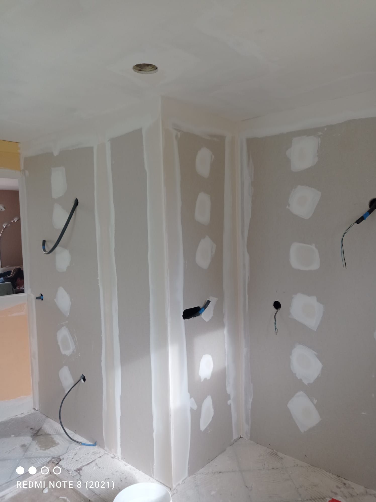 Pièce intérieure en travaux, avec murs et plafond en plaques de plâtre, câblage électrique apparent.