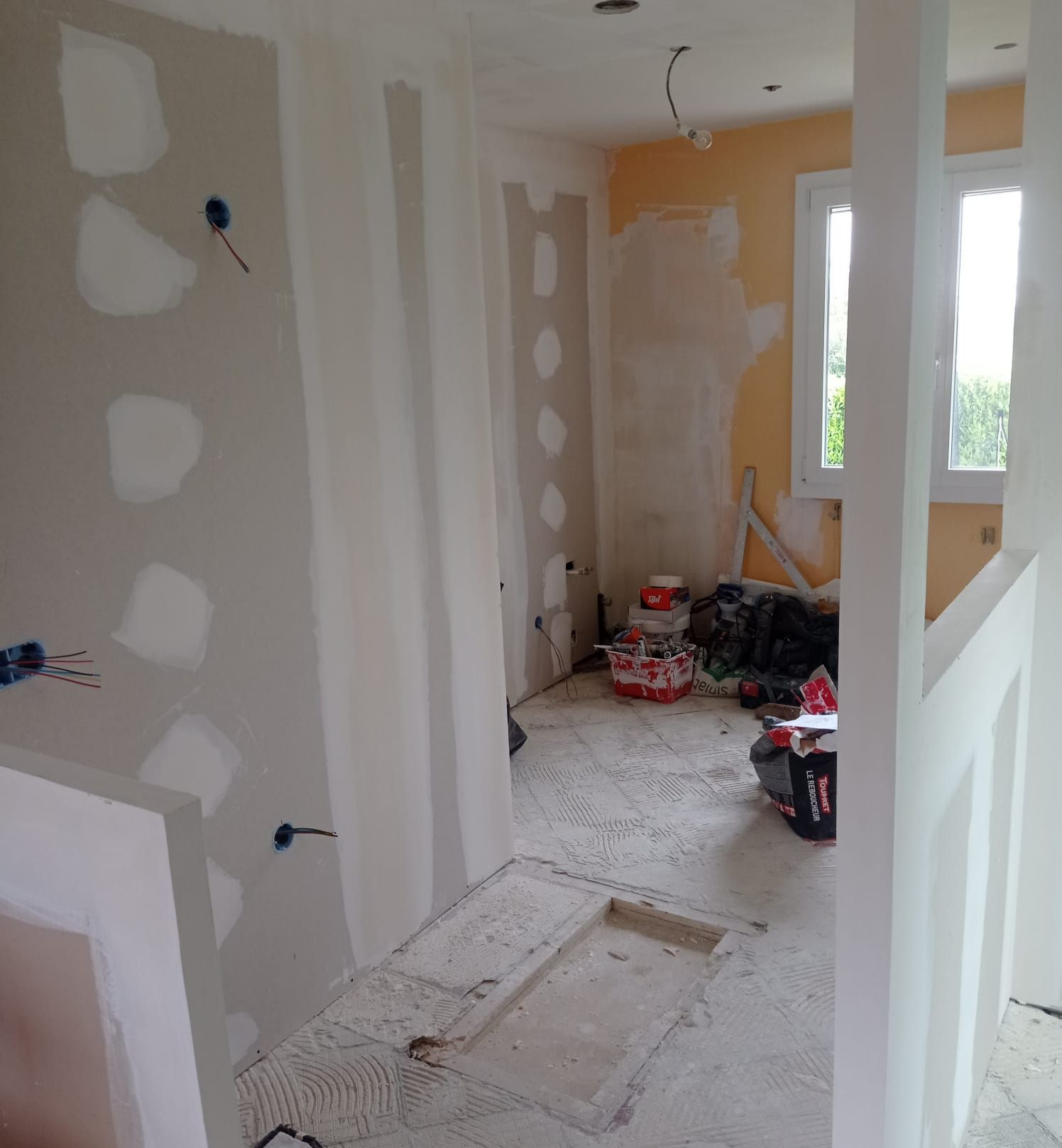 Vue intérieure d'une pièce en construction ; cloisons sèches partiellement posées, outils et matériaux divers éparpillés.