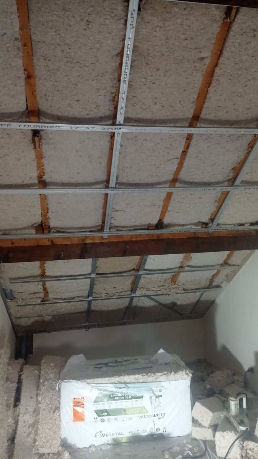 Vue intérieure d'une pièce avec poutres apparentes au plafond, une structure métallique et un grand sac au sol.