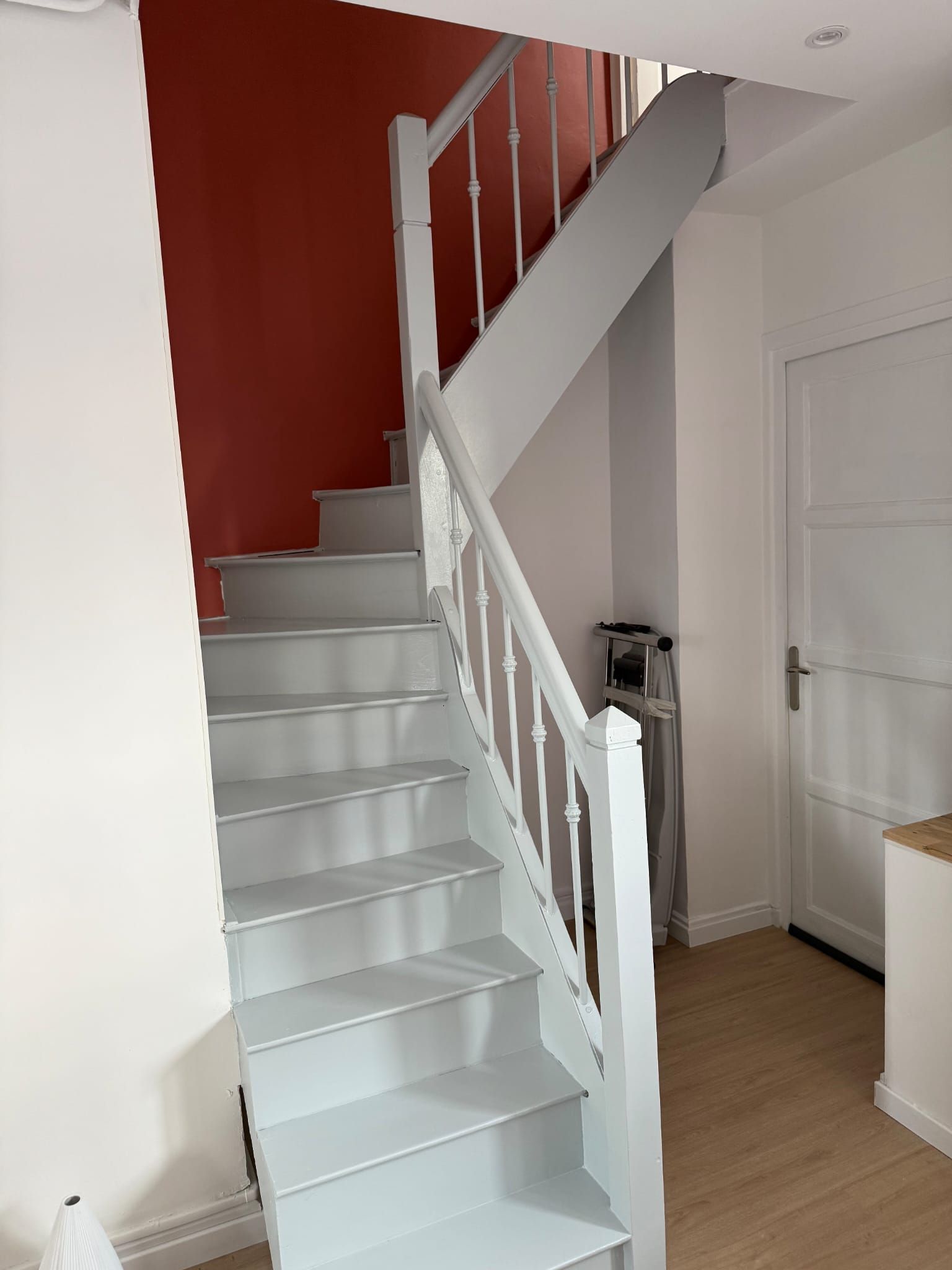 Escalier avec marches et rampe gris clair, mur d'accent rouge, murs blancs et porte blanche.