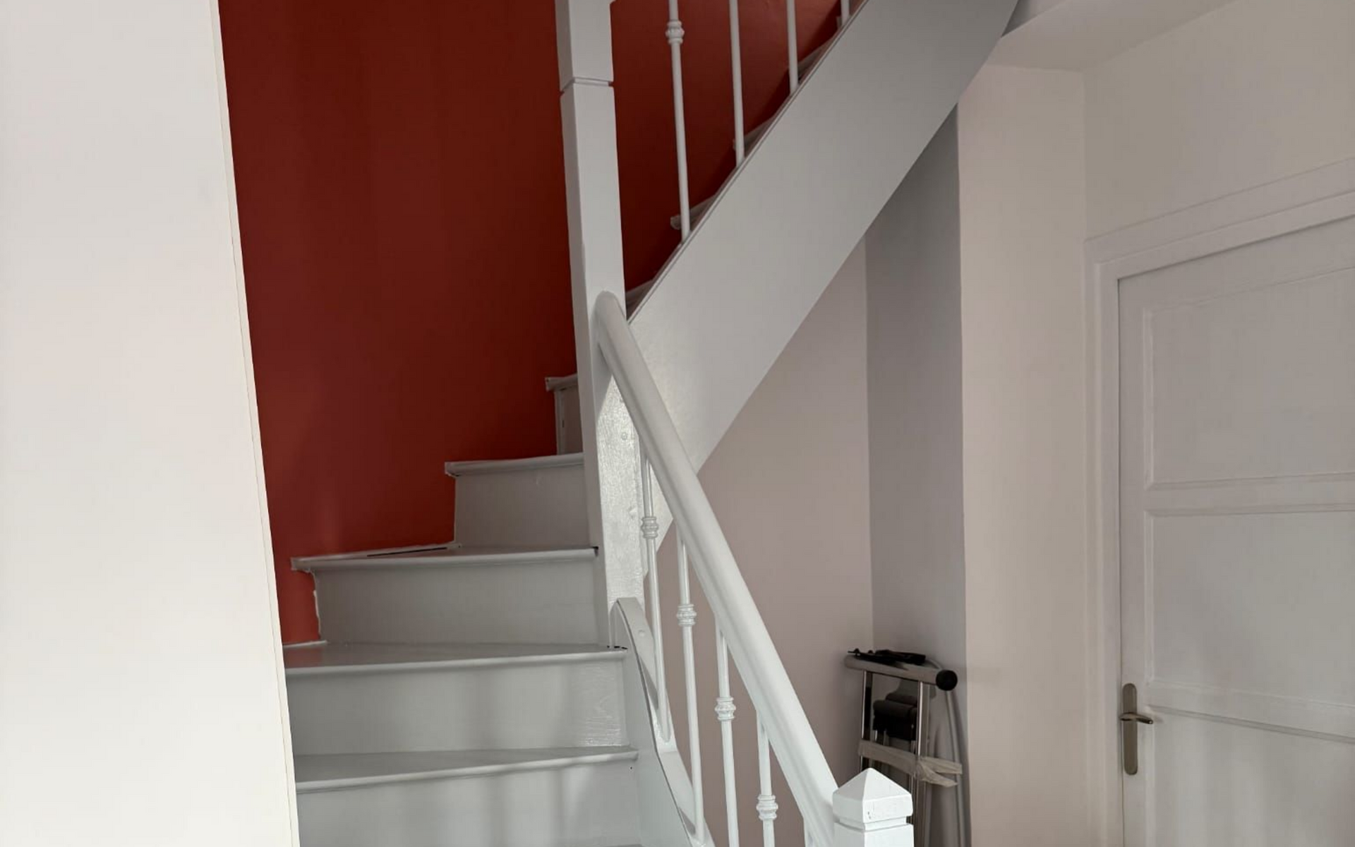 Escalier peint en blanc avec des marches grises sur des murs rouges et blancs.