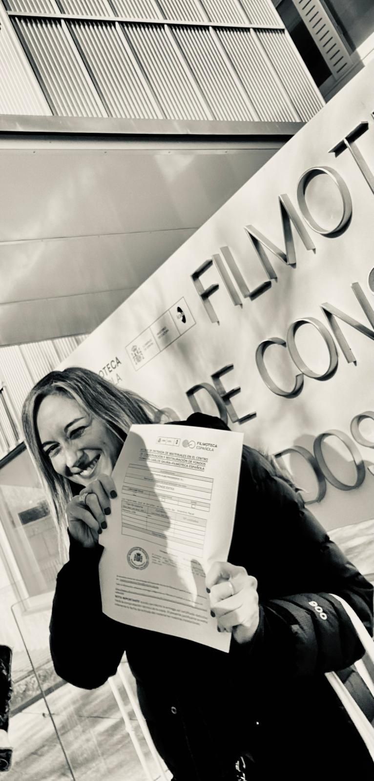 Mujer con boina y camisa amarillas mirando a través de binoculares dorados sobre un fondo amarillo.