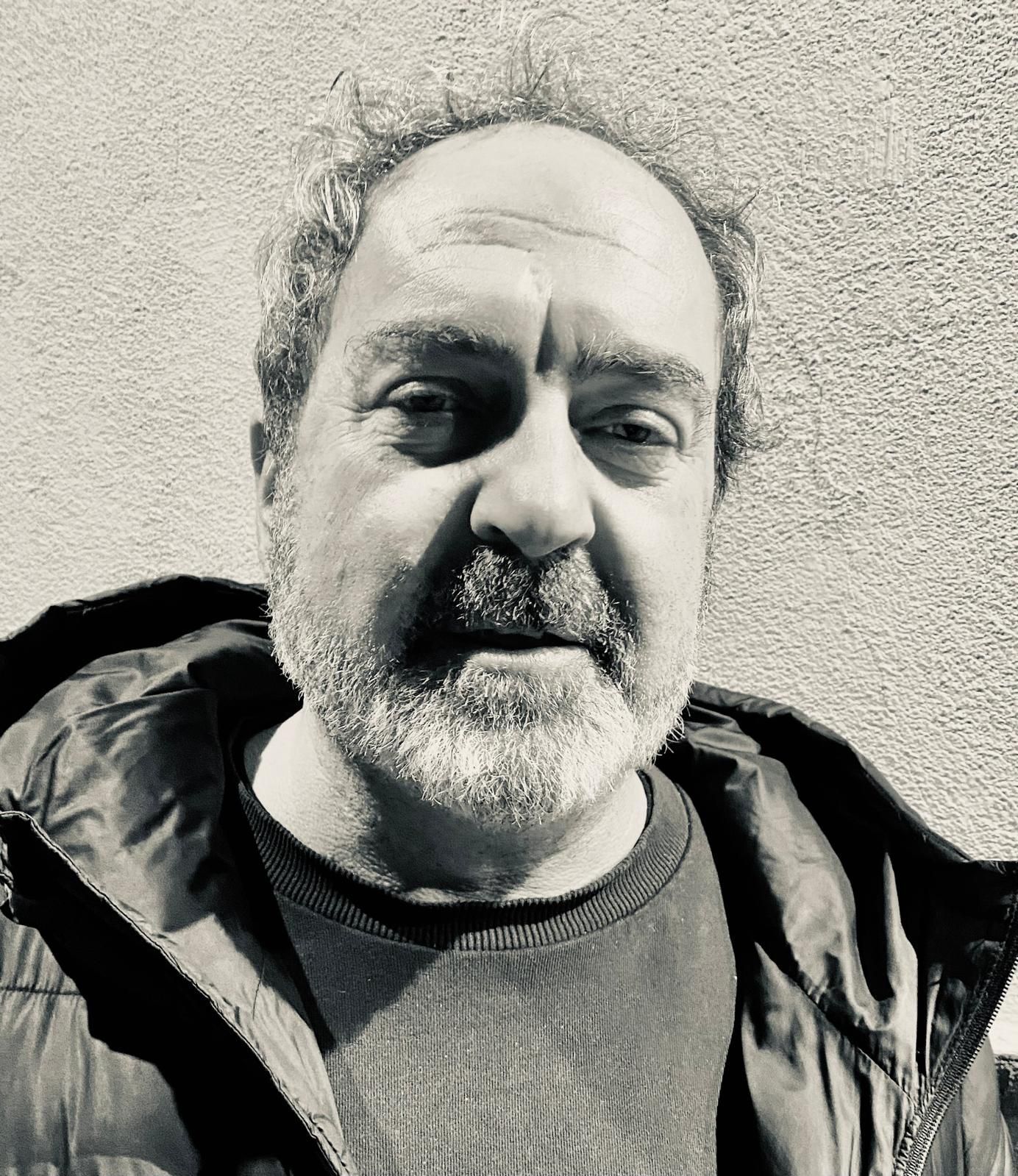 Mujer con los ojos cerrados sonríe, con la mano en el pelo, y lleva una blusa estampada. Fondo soleado de madera.