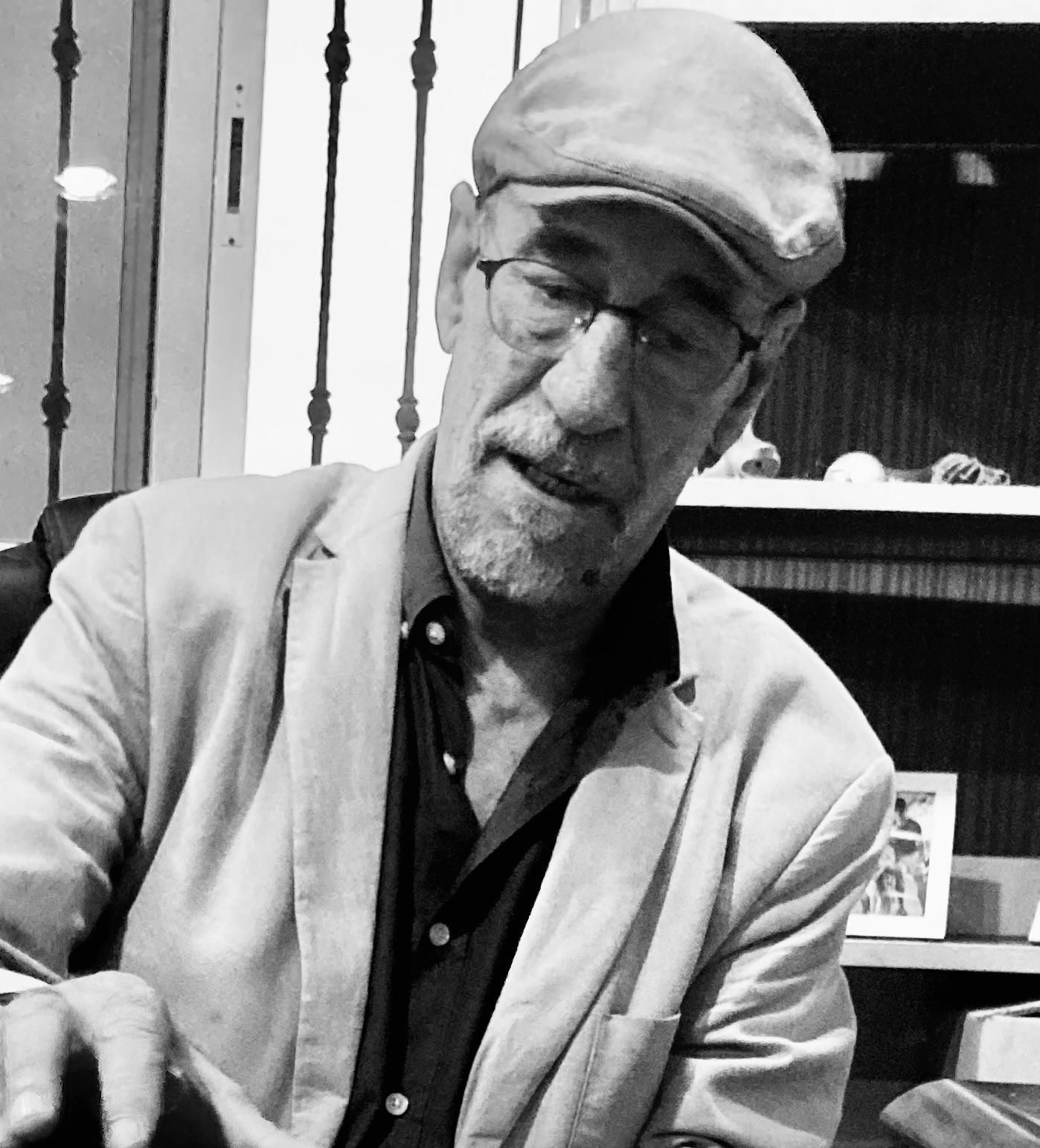 Hombre con gorra y gafas, sentado, vistiendo una chaqueta.