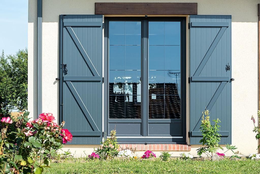 Photo de volets battants gris posés sur une porte-fenêtre