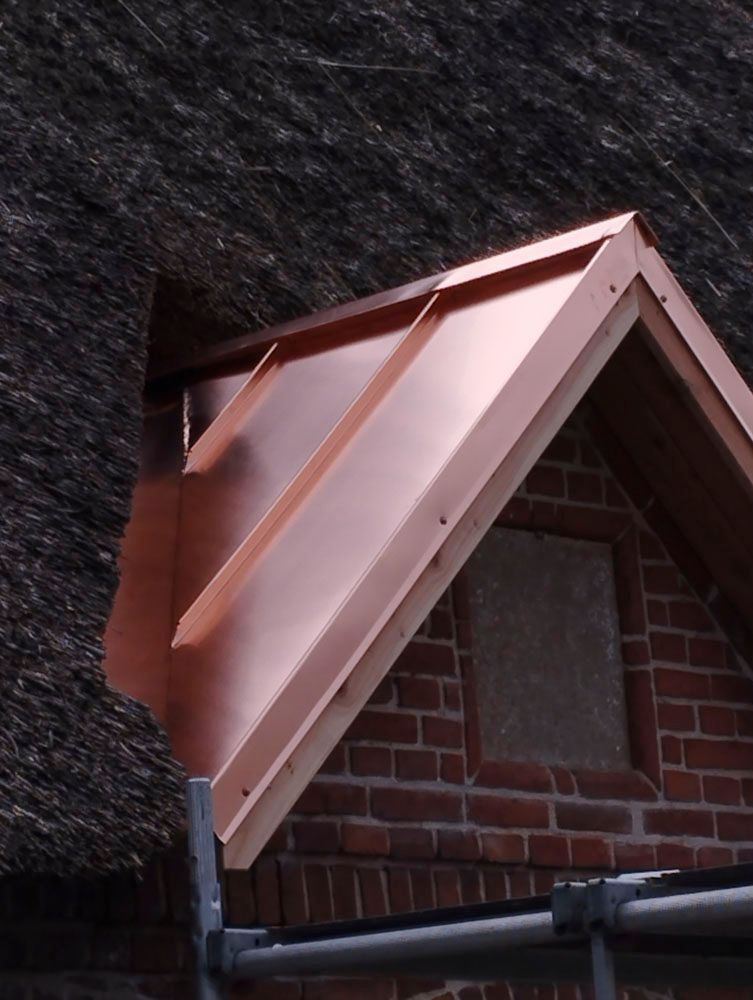 Kupferblechverkleidung an einem roten Backsteingiebeldach, angrenzend an ein Reetdach.